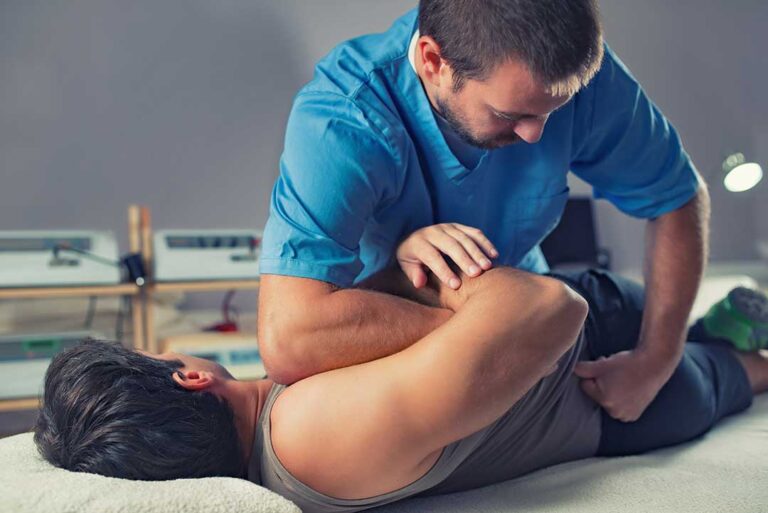 A young child and parent talking with a chiropractor in an exam room, with a spine model on the table nearby.